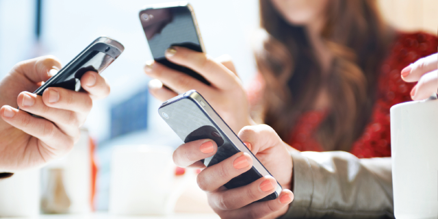 Three people using smartphones, focus on their hands and devices.